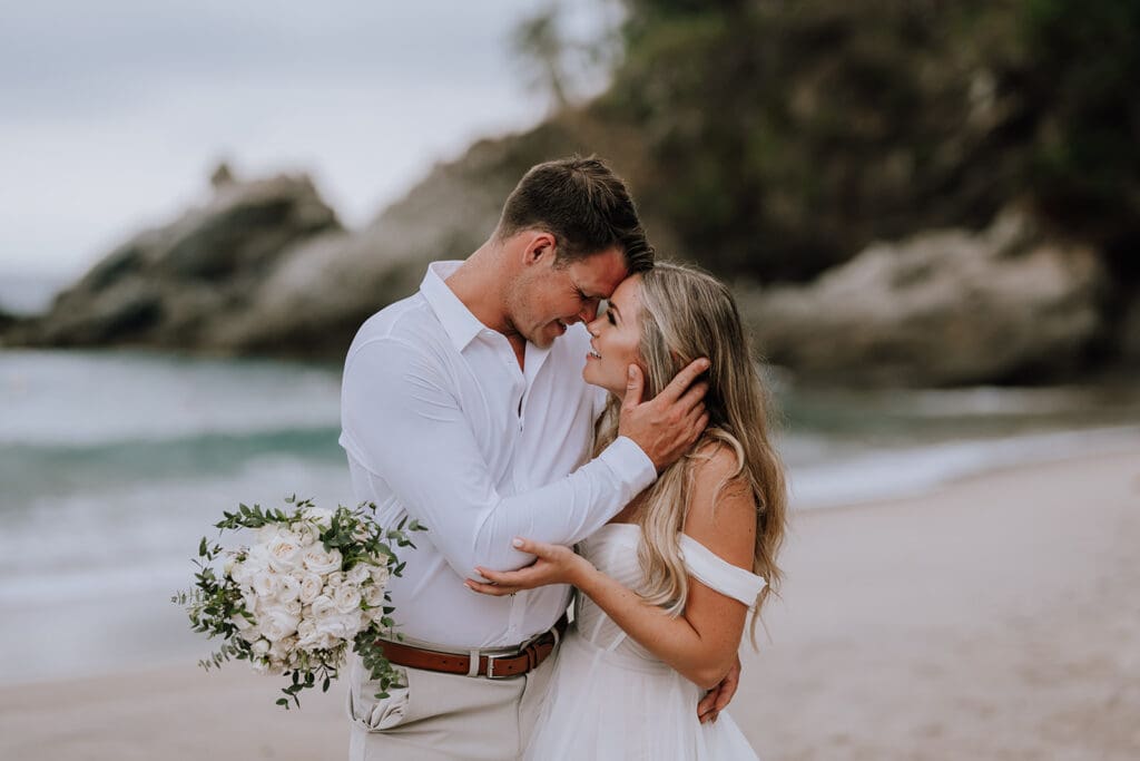 Hayley Zumkeller photography and videography team in Victoria BC capture a candid photo of a bride and groom during their beach wedding in an intimate embrace staring deeply and happily into each other's eyes.