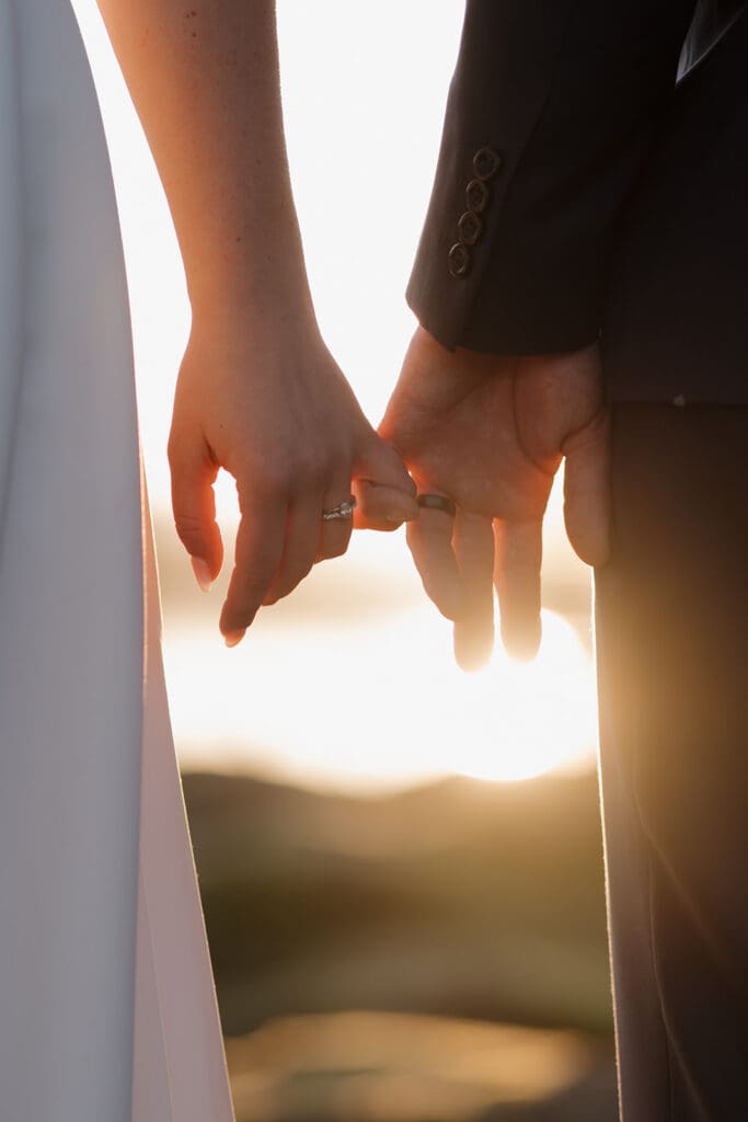 Hayley Zumkeller photography and videography team in Victoria BC capture the clasped pinky fingers of a newly married couple with the sun setting behind the image in a golden hour moment. 