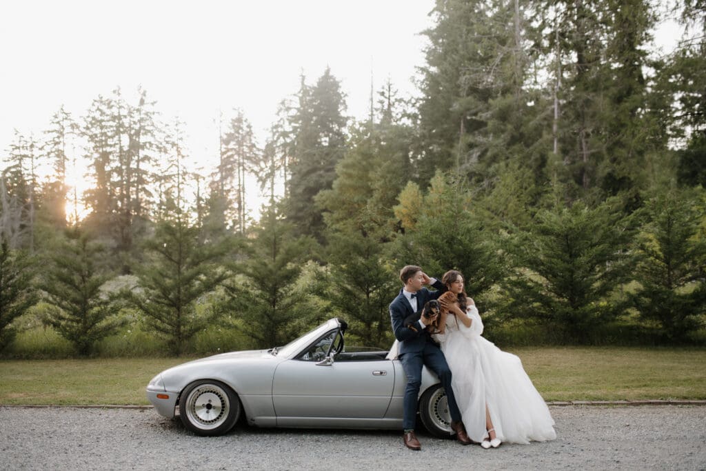 A newly married couple and their dogs pose for photos to be captured by Hayley Zumkeller photography and videography team as they stand beside a convertible on Vancouver Island.