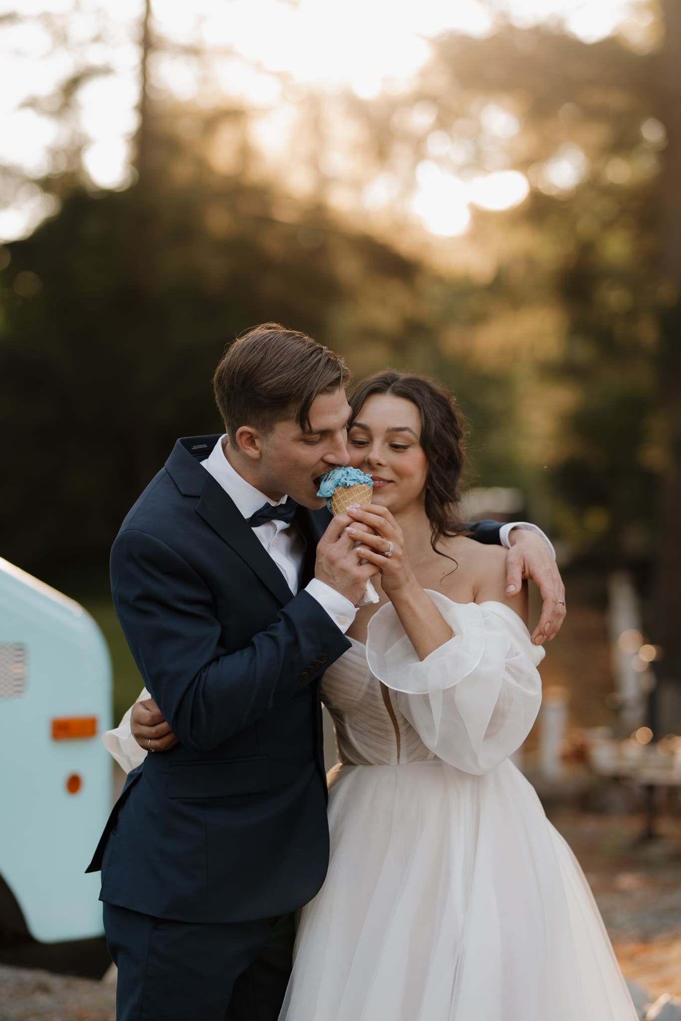 Hayley Zumkeller photography and videography team capture a husband and wife sharing an ice cream cone following their wedding, with the golden hour rays filtering through the trees in the background.