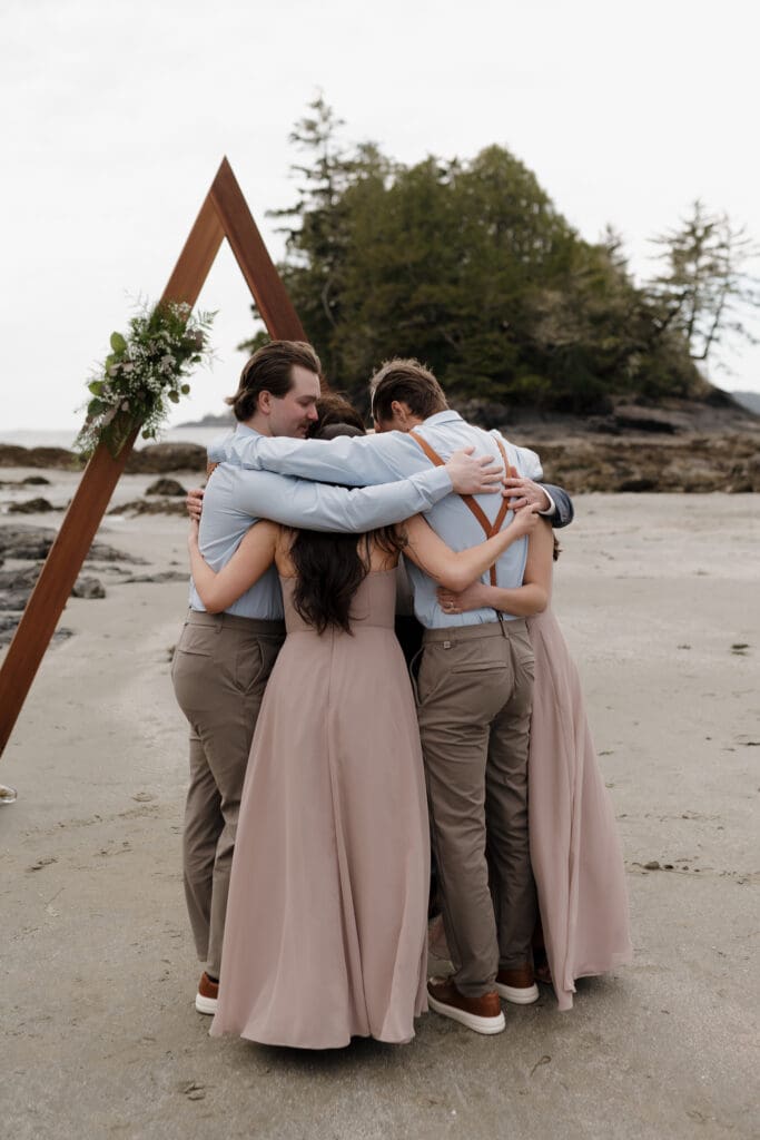 An intimate elopement on Chestman Beach in Tofino BC. The family all embrace in a huddle on the beach following the celebration.  Local Tofino BC Wedding Photographer captures moments on both photo and video