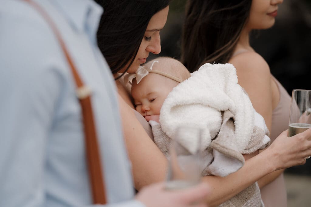 The baby granddaughter of the Bride in her mother's arms during the elopement ceremony at Crystal Cove Beach Resort at Chesterman Beach. Local Tofino BC Wedding Photographer captures moments on both photo and video.
