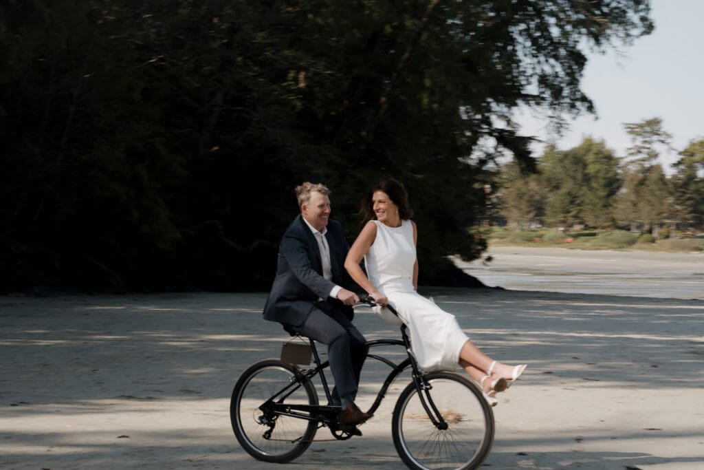 Tofino BC Wedding Photographer and Videographer captures bride and groom after their wedding ceremony at Crystal Cove Resort on Chesterman Beach. Couple rides bike on the beach.