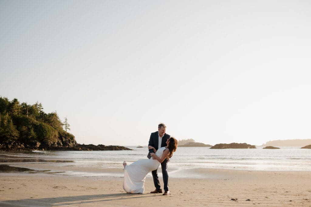 Hayley Zumkeller photography and videography team capture an image of a new husband dipping his new wife for a kiss following their elopement on Chesterman Beach on Vancouver Island in BC.