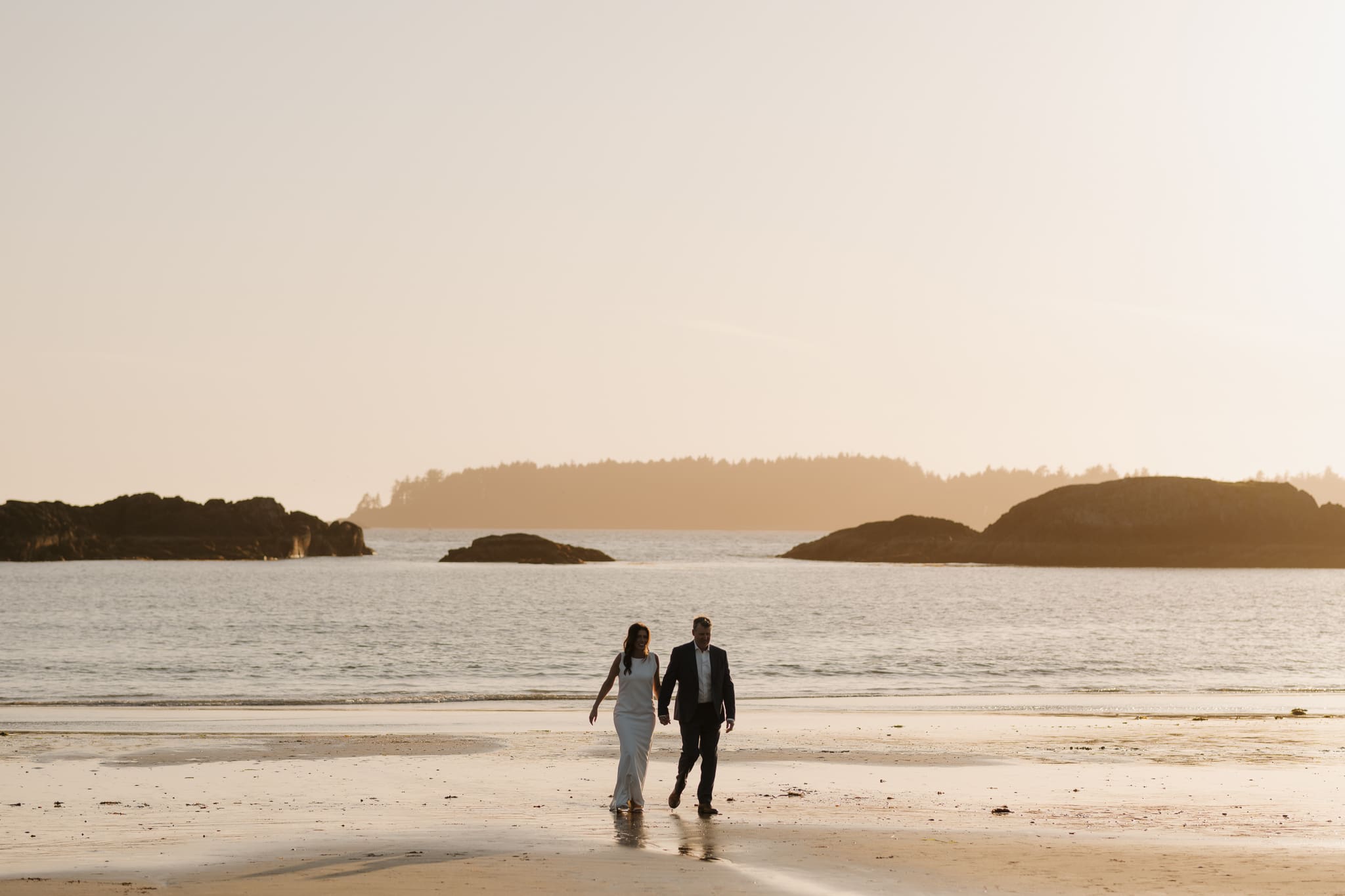 Tofino BC Wedding Photographer and Videographer film a Tofino Wedding Video for an intimate, elegant wedding on Chesterman Beach at Crystal Cove Resort. Photos of bride and groom at sunset walking in the distance along chesterman beach
