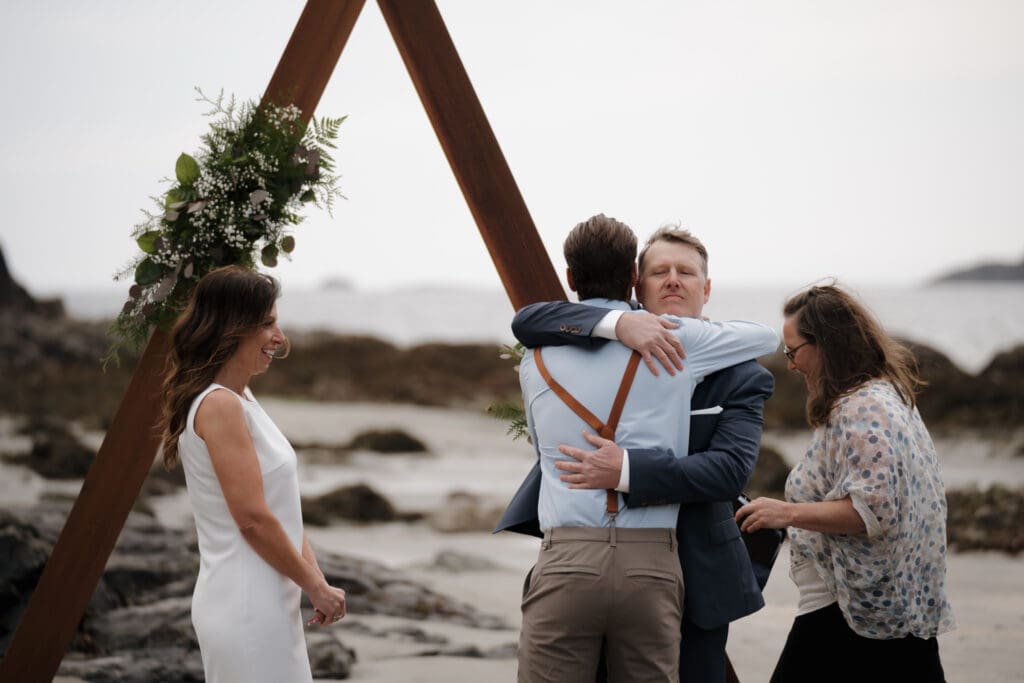 The son of the Groom embraces his Dad following the elopement ceremony at Crystal Cove Beach Resort at Chesterman Beach. Local Tofino BC Wedding Photographer captures moments on both photo and video.