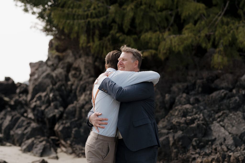 Vancouver Island photography and videography team capture a groom embracing his son outside at their Chesterman Beach elopement ceremony in Tofino BC.