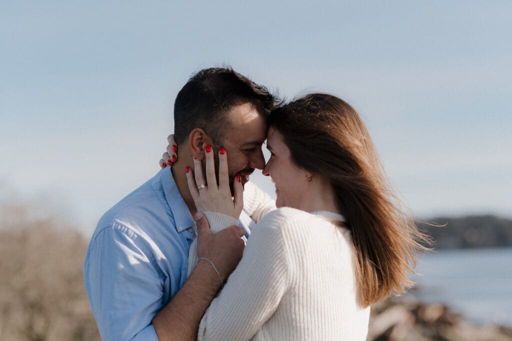 Hayley Zumkeller photography and videography team from Victoria BC capture a surprise proposal on Vancouver Island. The couple in this close up image are smiling lovingly at each other, their foreheads touching, as the blue sky beaches stretch out behind them.