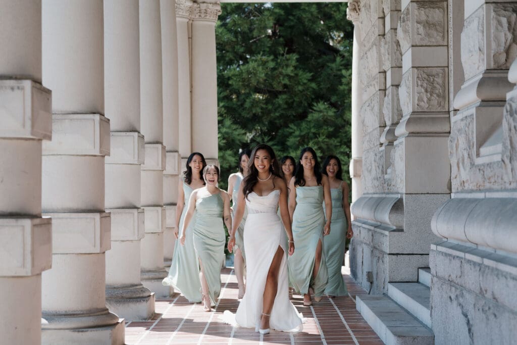Hayley Zumkeller, Victoria BC Wedding Videographer and Photographer captures a bride walking toward the camera with her bridesmaids walking behind her in elegant light green gowns at Parliament grounds in Victoria BC on Vancouver Island.