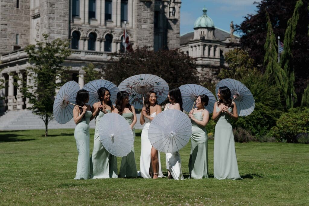 Hayley Zumkeller, Victoria BC Wedding Videographer and Photographer and team capture a distance shot of the bride and bridesmaids with their parasols during wedding party photos on the Parliament grounds on Vancouver Island.