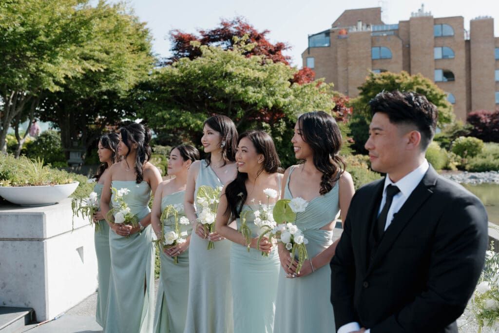 Hayley Zumkeller Photography and Videography team from Victoria BC capture a groom and the bridesmaids as they watch the bride come down the aisle during an outside ceremony at Laurel Point Inn on Vancouver Island for their mini-destination wedding.