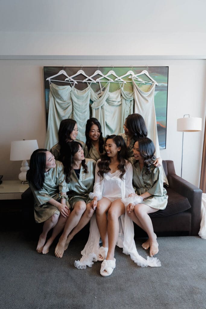 Hayley Zumkeller, Vancouver Island Wedding Videographer and Photographer captures a bride getting ready with her bridesmaids, all in matching robes and slippers (the bride in white and the bridesmaids in light green) as they pose for a getting ready photo at Laurel Point Inn in Victoria BC