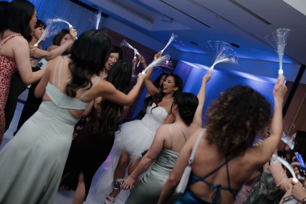 Hayley Zumkeller, Victoria BC Wedding Videographer and Photographer captures the high energy dance party at a wedding reception at Laurel Point Inn in Victoria BC. The bride is surrounded by friends with sparklers, laughing and having a great time.