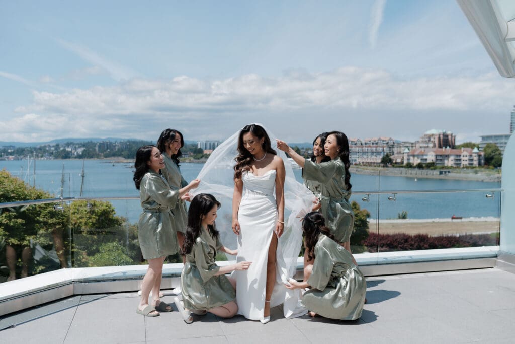 Hayley Zumkeller, Vancouver Island Wedding Videographer and Photographer captures a bride with her bridesmaids, in their wedding dresses as they pose together for a patio photo at Laurel Point Inn in Victoria BC