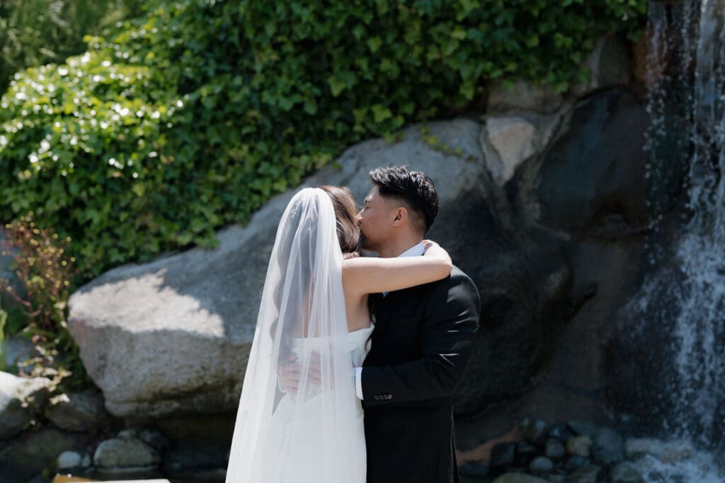 Hayley Zumkeller Photography and Videography team from Victoria BC capture a groom kissing his bride during their first look at the waterfall feature on the grounds of Laurel Point Inn on Vancouver Island