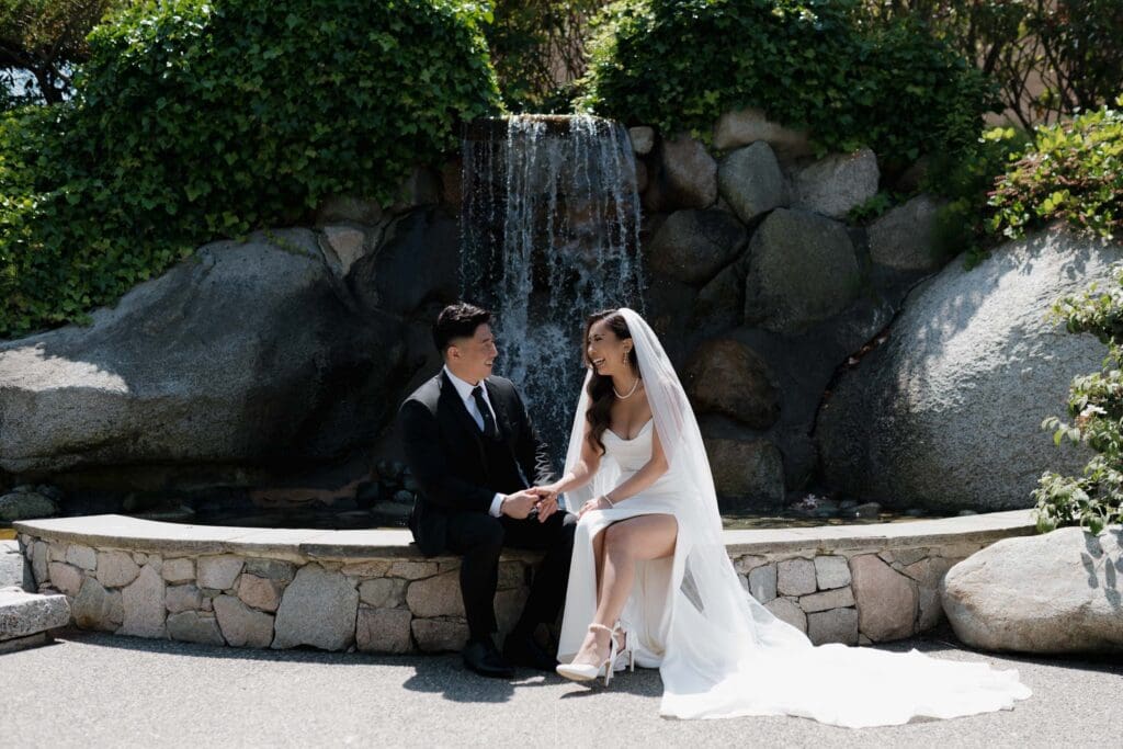 Hayley Zumkeller Photography and Videography team from Victoria BC capture a bride and groom smiling at each other during their first look at the waterfall feature on the grounds of Laurel Point Inn on Vancouver Island