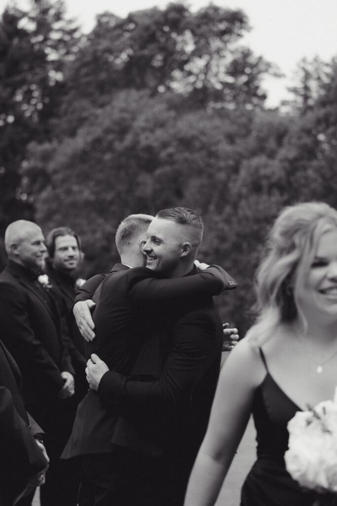 Hayley Zumkeller photography and videography team from Victoria BC capture the groom just prior to the start of the ceremony hugging his best man with the at Olympic View golf course in Victoria BC on Vancouver Island in the background in this black and white image.
