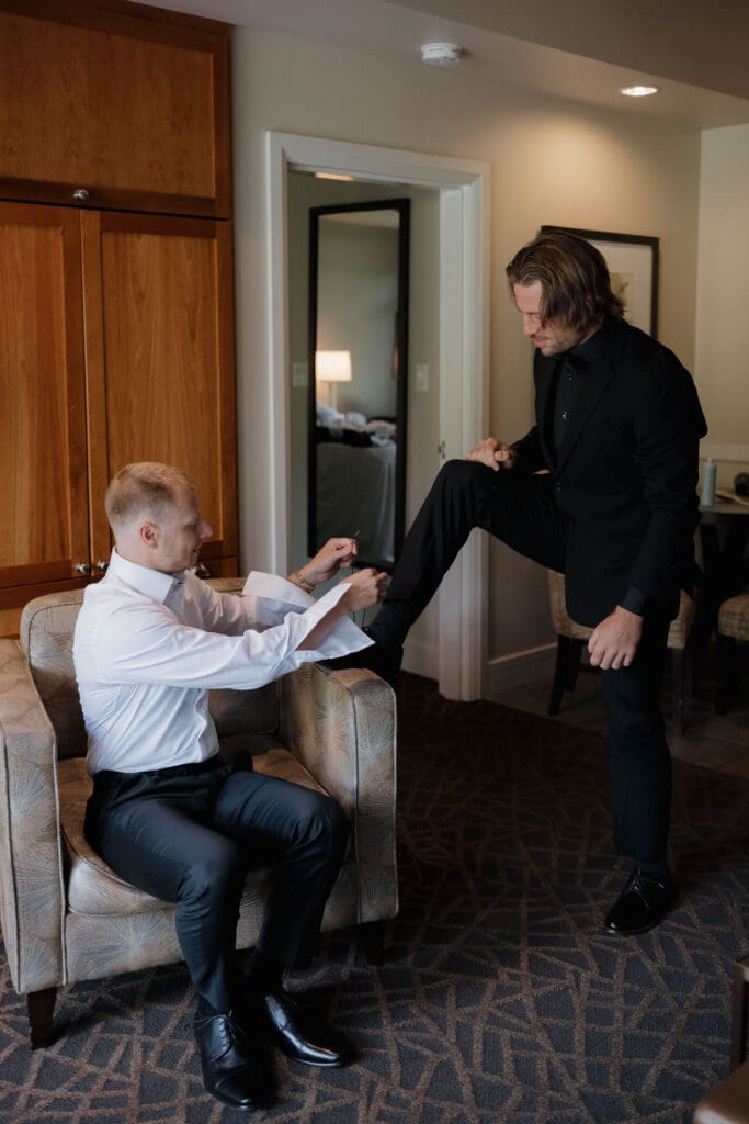Hayley Zumkeller Photography & Videography team from Victoria BC capture a groom getting ready for the ceremony helping one of the groomsman tie his shoes.