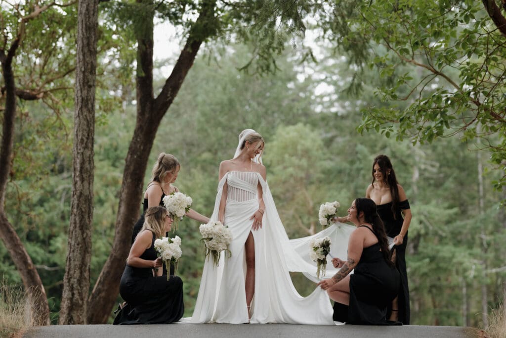 Hayley Zumkeller photography and videography team from Victoria BC capture an elegant image of a bride with her bridesmaids among the tree at Olympic View Golf Course. The bride is in the centre as her bridesmaids arrange her dress.