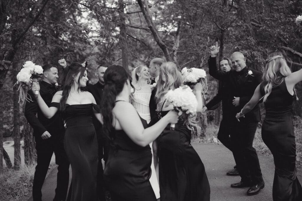 Hayley Zumkeller Photography and Videography team from Victoria BC capture a black and white image of the bride and groom among the trees at Olympic View Golf Course. They are staring deeply into each other's eyes with smiles on their face as the wedding party dances around them.