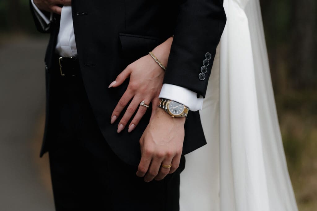 Hayley Zumkeller photography and videography team from Victoria BC capture a bride embracing her husband from behind. We see their left hands with new wedding bands on display.
