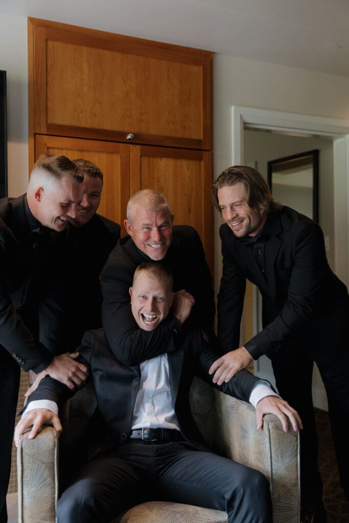 Hayley Zumkeller photography and videography team from Victoria BC capture getting ready photos for a wedding day at Olympic View Golf Course. In this image the groom surrounded by the men of his family in a fun loving headlock during pre-ceremony antics.