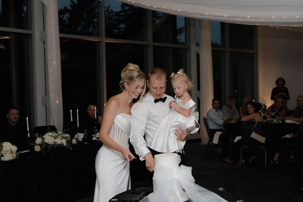 Hayley Zumkeller Photography and Videography team capture a bride and groom cutting the cake with their daughter in their arms. The joining not just of two people, but of a family. Shot at Olympic View Golf Course on Vancouver Island BC.