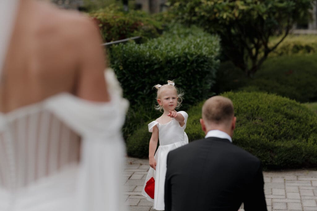 Hayley Zumkeller photography and videography team from Victoria BC capture the first look moment between a bride and groom, joined by their daughter as the daughter points out her mom standing behind her dad in this heartwarming image of a family joining together.