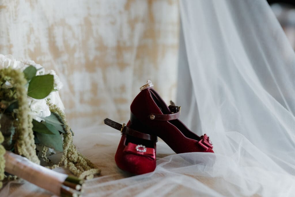 Hayley Zumkeller photography and videography team from Victoria BC capture the flowergirl's red shoes atop the bride's veil with the engagement ring on top and a white bouquet beside.