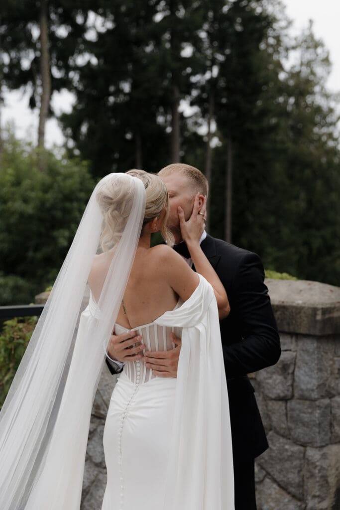 Hayley Zumkeller photography and videography team from Victoria BC capture the first look kiss between a bride and groom. Her elegant gown and flowing veil and gown caught in his romantic embrace.