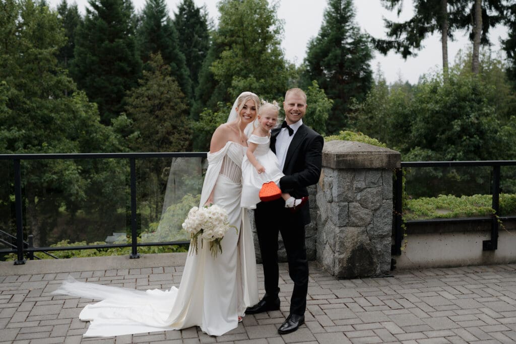 Hayley Zumkeller photography and videography team from Victoria BC capture the moment just following the first look, as the bride and groom are joined by their daughter, smiling together as a family toward the camera.