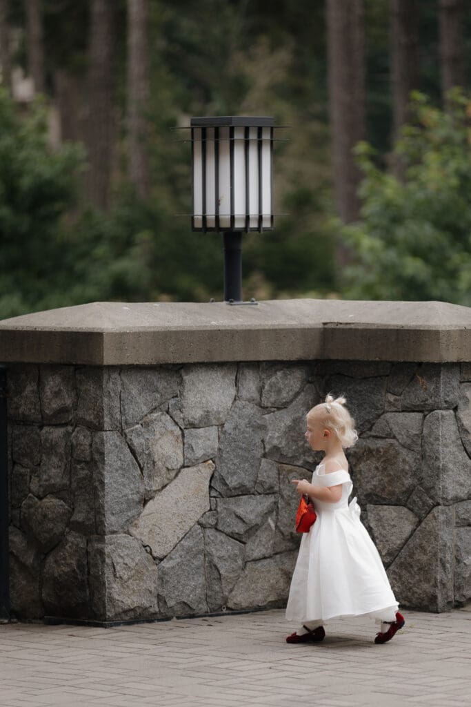 Hayley Zumkeller photography and videography team from Victoria BC capture the daughter of a bride and groom watching the first look between her parents. Her red purse and red shoes contrasted by her white satin gown.