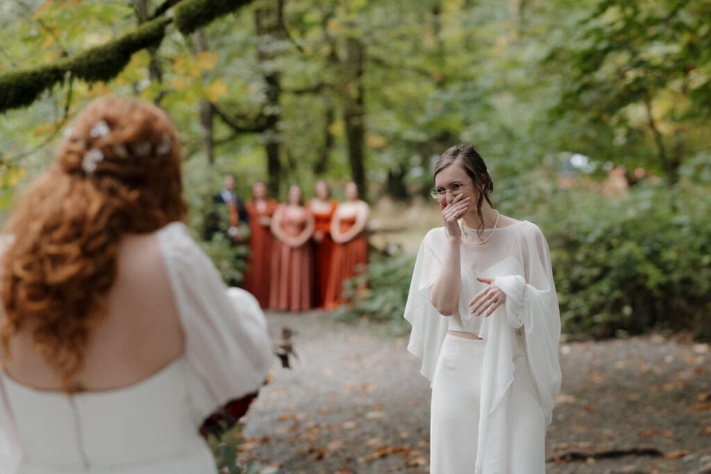 An emotional first look is captured by Hayley Zumkeller photography and videography team on Vancouver Island, with the bridesmaids in the background in their vivid fall coloured dresses.