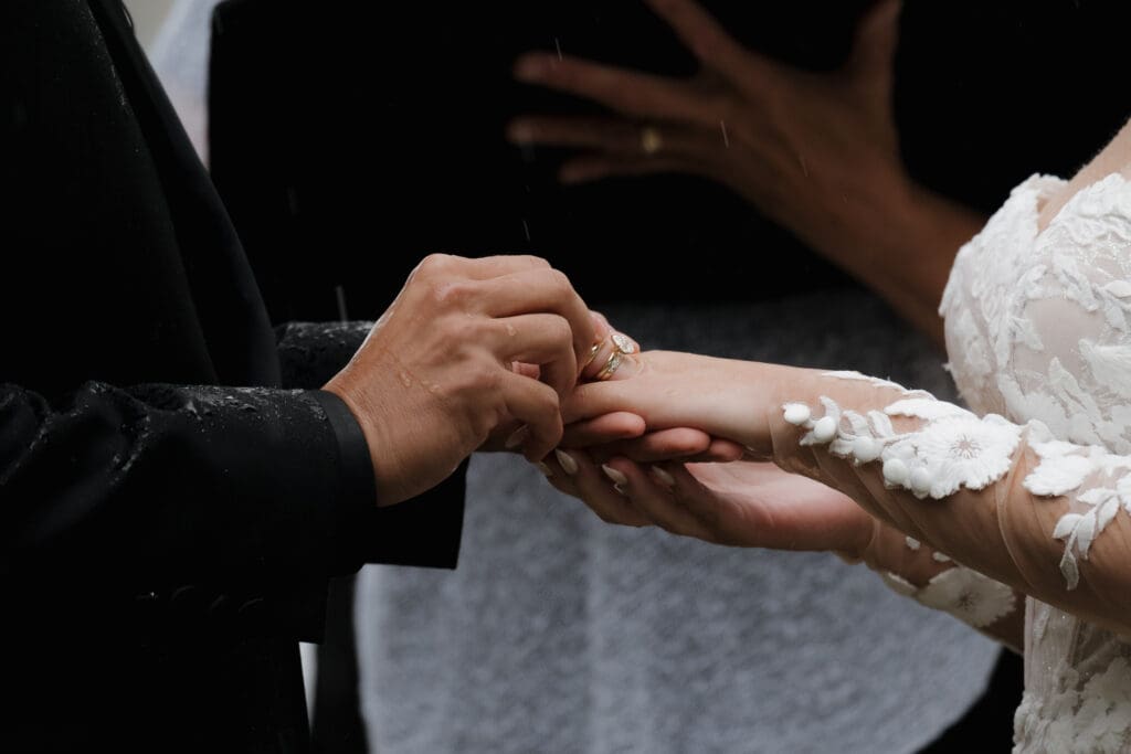 Hayley Zumkeller photography and videography team captures the exchanging of rings during a Gowlland Harbour Wedding on Vancouver Island. We see the groom placing the wedding band on his bride's finger and the drops of rain on both their hands.