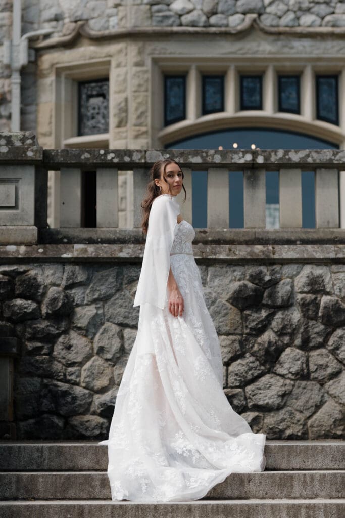 A bride on her wedding day with the historical Hatley Castle in the background in Victoria BC. Her breathtaking dress, topped with an elegant shawl, on full display. Image captured by Hayley Zumkeller photography and videography team.
