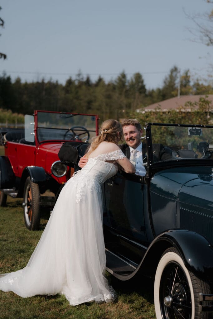 Hayley Zumkeller photography and videography team capture the bride leaning over the antique car to kiss her new husband. You can see another red antique car in the background.