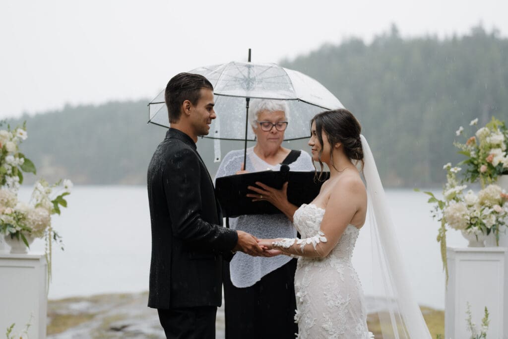 A BC officiant performs the wedding ceremony of a bride and groom on Vancouver Island. Amidst the rain. Image captured by the talented Hayley Zumkeller photography and videography team from Victoria BC.