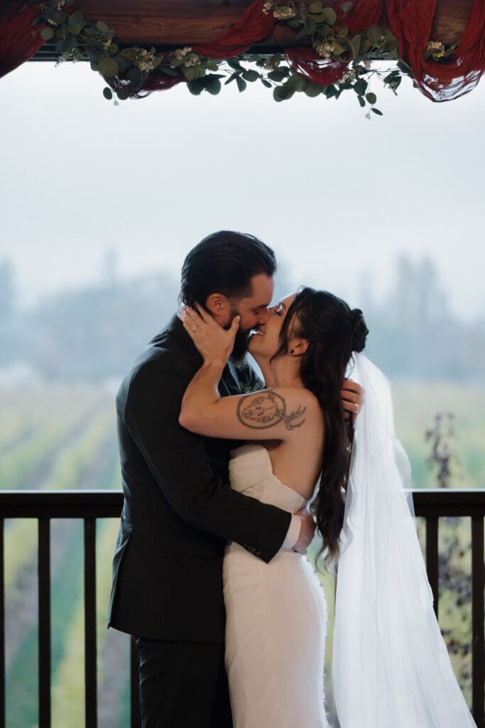 Hayley Zumkeller photography and videography team from Victoria BC captures a first kiss by a bride and groom during this misty fall wedding at Church and State Winery on Vancouver Island.