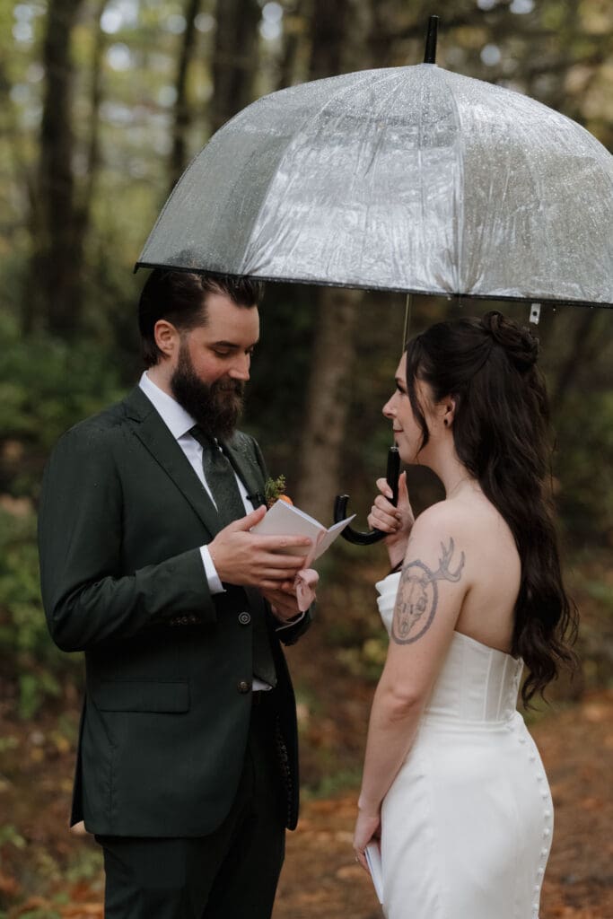 Hayley Zumkeller photography and videography team from Victoria BC capture a private moment between a bride and groom under an umbrella in the light rain, surrounded by the forestry at Church and State Winery on Vancouver Island.