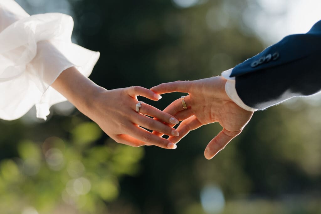 Hayley Zumkeller photography and videography team from Victoria BC capture a bride and groom reaching their hands toward each other with lush greenery of Puska Properties in Nanaimo in the background.