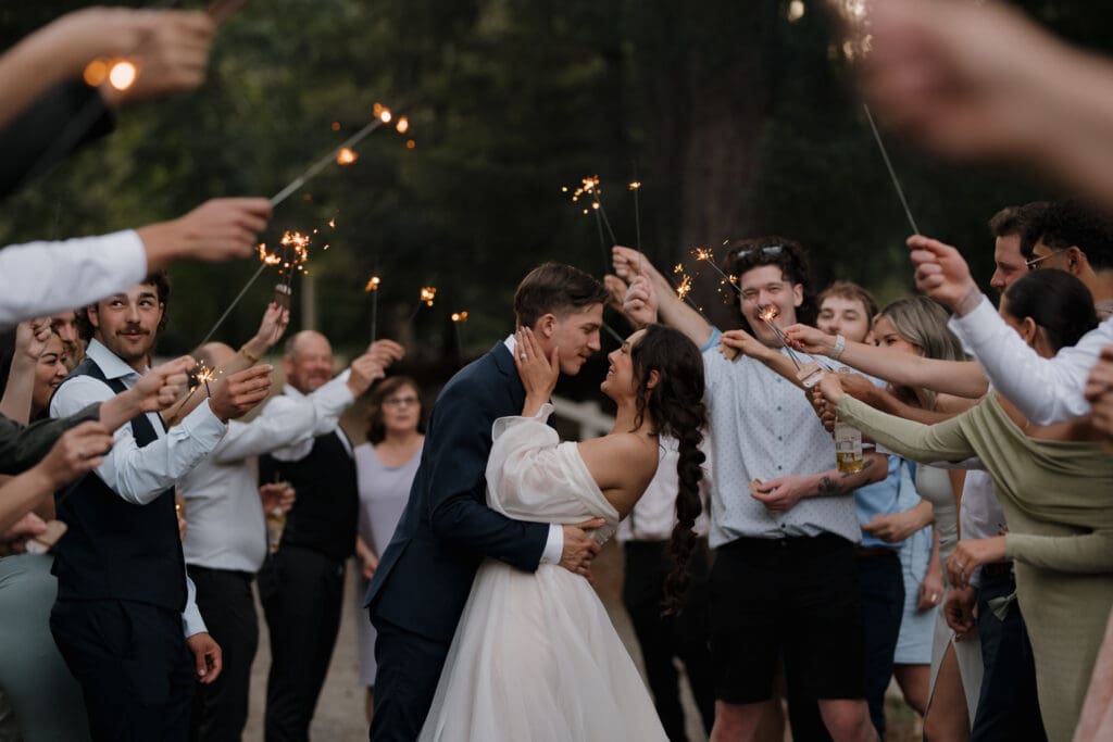 Hayley Zumkeller photography and videography team from Victoria BC capture a bride and groom kissing surrounded by their guests during a sparkler exit. 