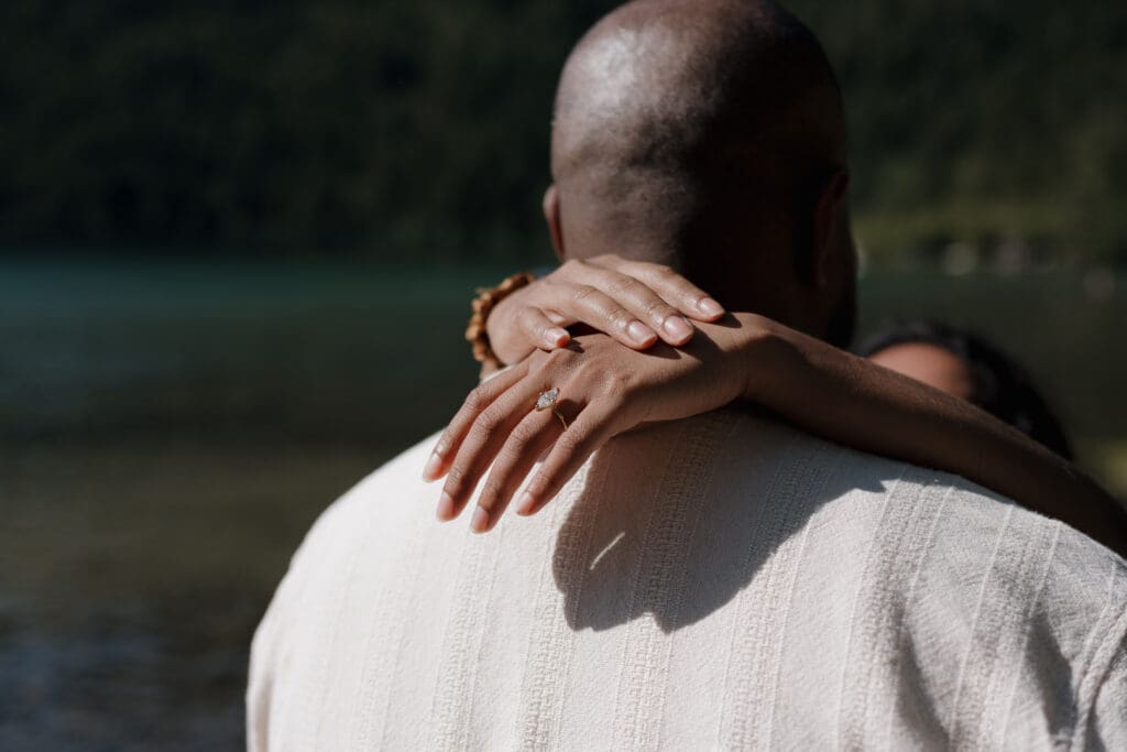 Hayley Zumkeller, a Victoria BC photographer, captures the engagement ring between clasped hands encircling the neck of her new fiance in an intimate embrace following her surprise proposal at Cameron Lake on Vancovuer Island.