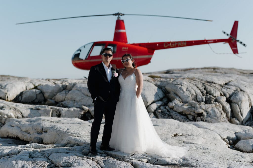 Bride and groom standing beside red helicopter during mountain top elopement on Vancouver Island