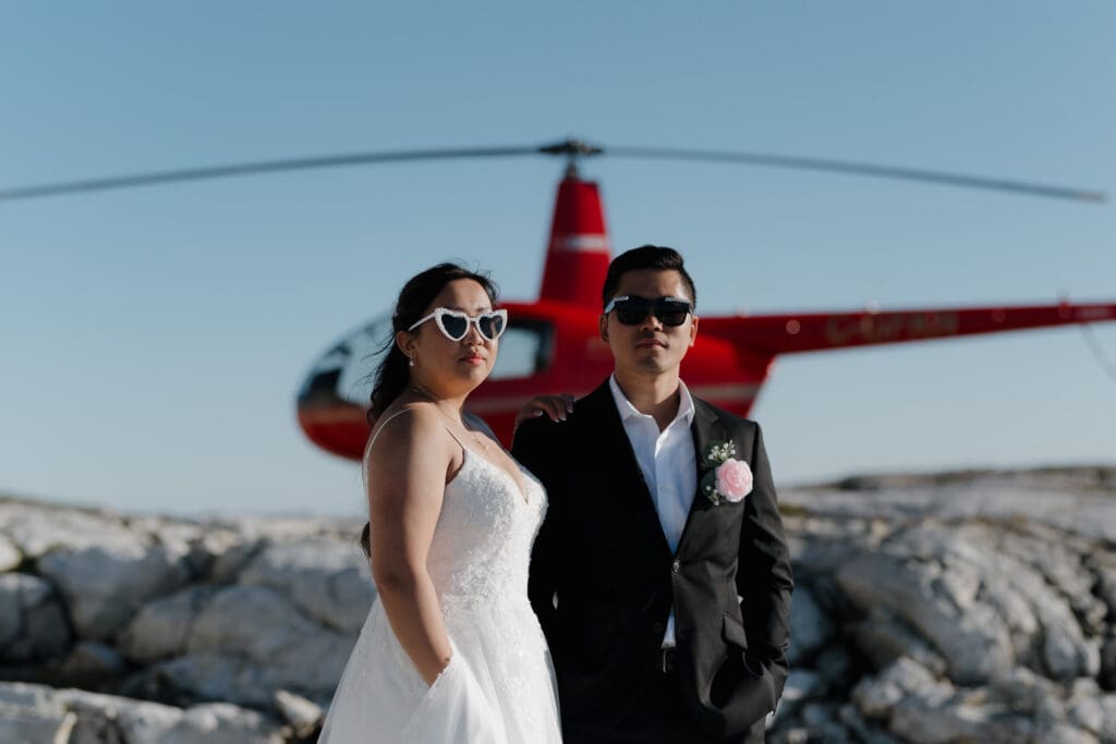 Bride and groom standing beside red helicopter during mountain top elopement on Vancouver Island