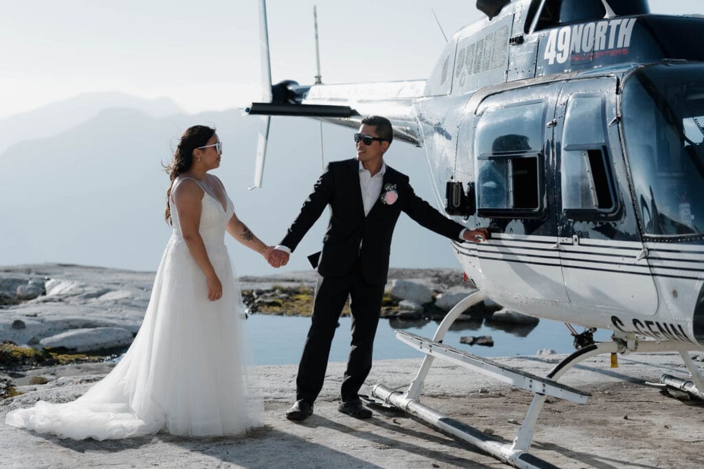A groom opening the helicopter door for his bride, about to take off for their mountain top elopement on Vancouver Island. Moment captured by Hayley Zumkeller photography and videography team from Victoria BC.