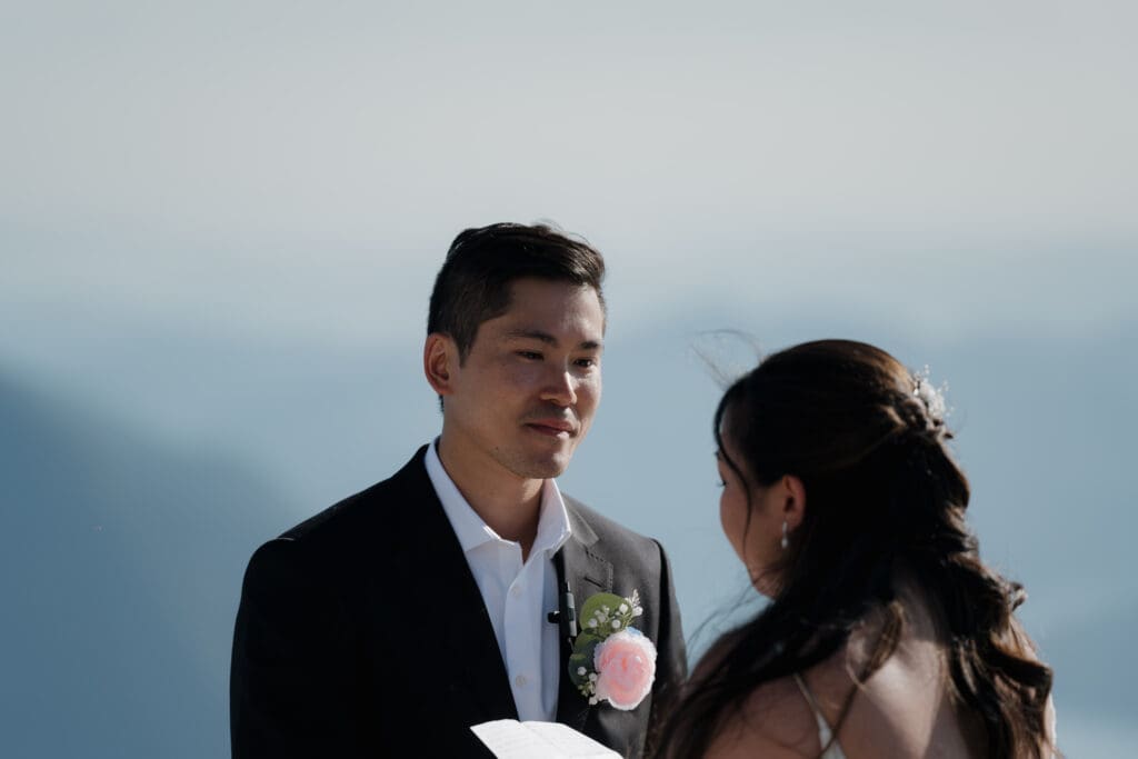 Image of a groom holding back tears as his bride says her vows on a mountaintop on Vancouver Island for their Helicopter Elopement.