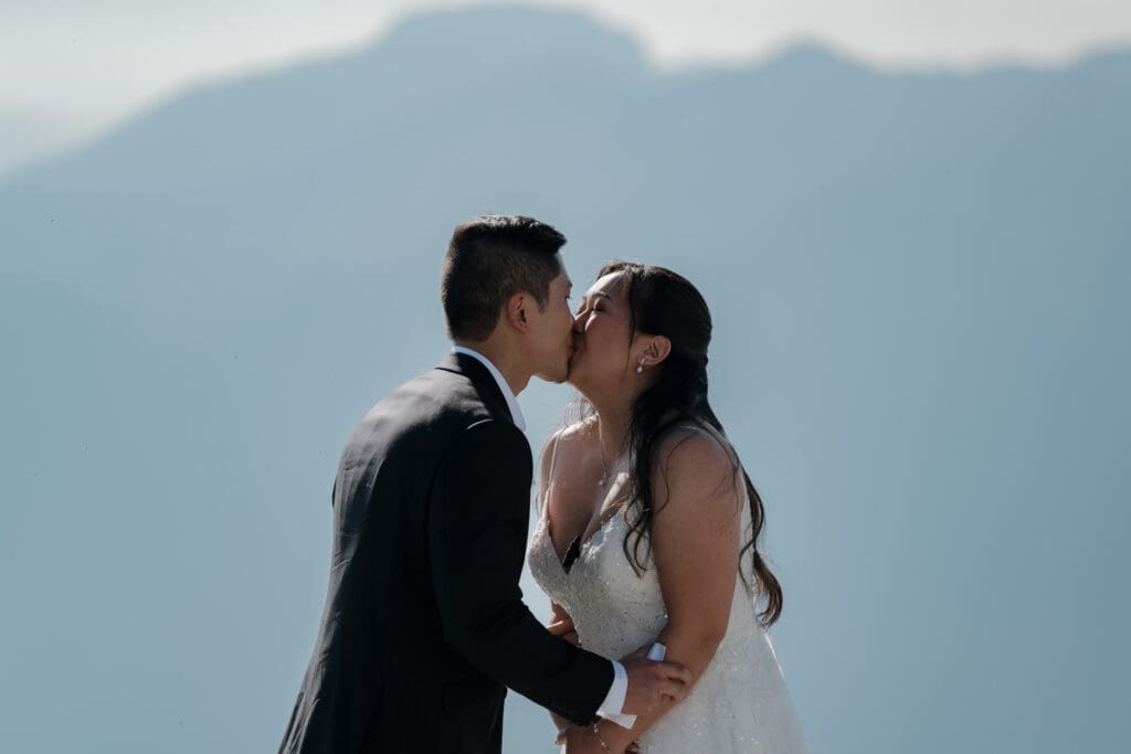 Bride and groom share their first kiss as husband and wife on mountain top during cinematic helicopter elopement Vancouver Island.