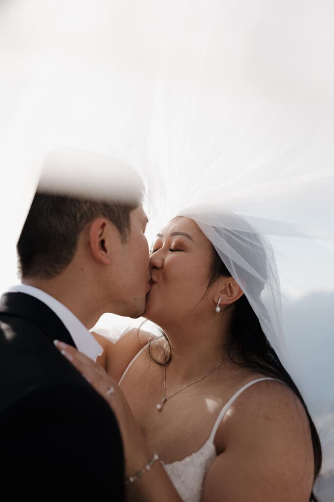 Romantic veil moment between bride and groom during mountain top elopement in British Columbia.