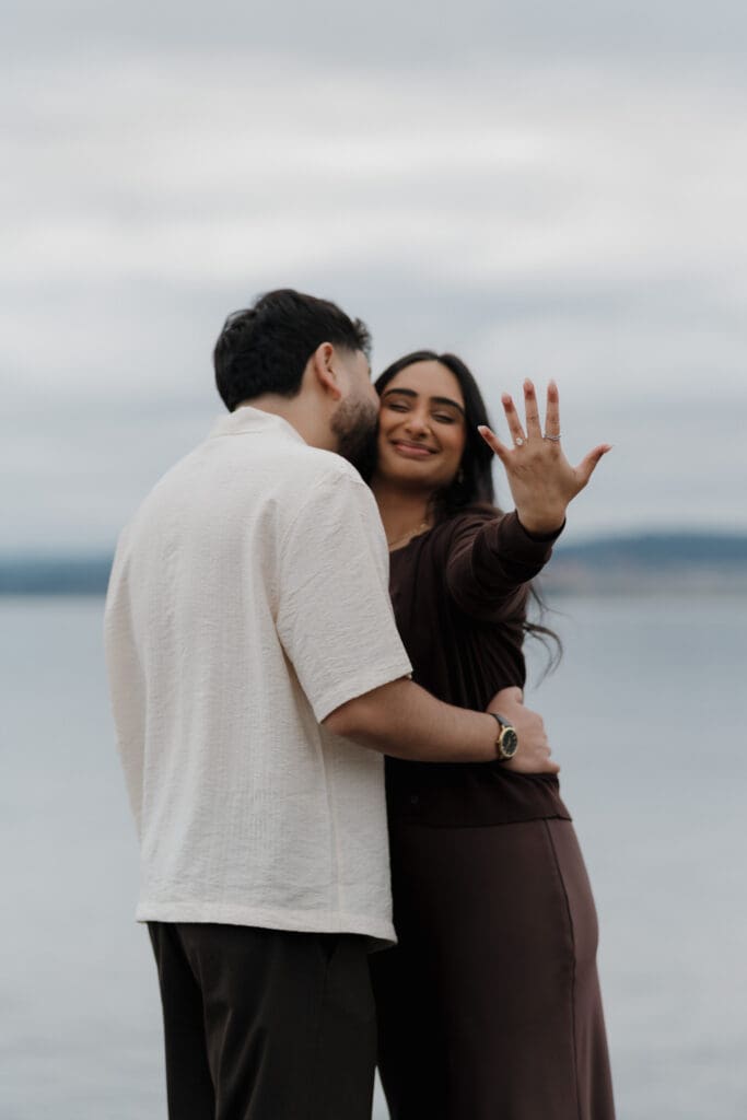 Newly engaged couple walking along the shoreline at Saxe Point Park in Esquimalt, Victoria BC after surprise proposal