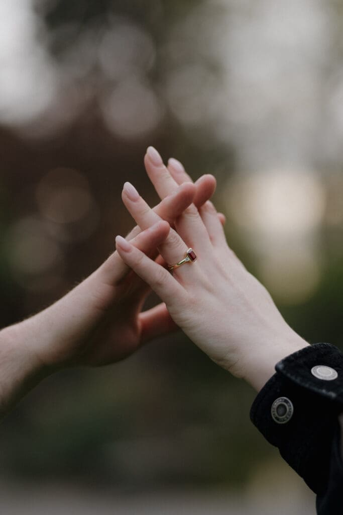 A newly engaged couple from Vancouver Island with clasped hands showing the stunning and unique ruby engagement ring.